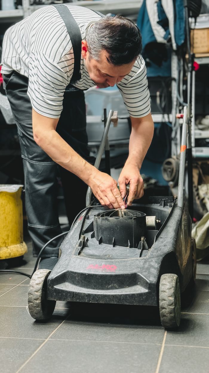 Adult repairing a lawn mower in a garage workshop, focused on maintenance and DIY repair.